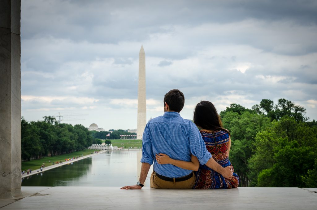 photo of a couple with their backs to the camera sitting and looking at the Washington Monument in the distance