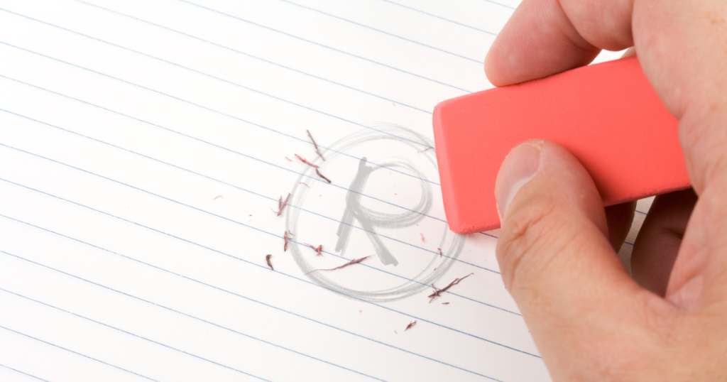 close up of a hand holding an eraser and erasing a trademark symbol