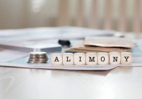 Word,Alimony,Composed,Of,Wooden,Letters.,Closeup with stack of coins