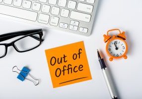 note with out of office written on it sitting on a desk surrounded by office supplies