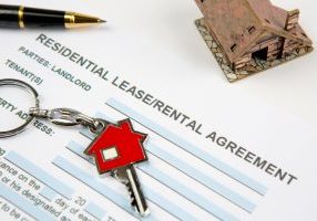 Lease agreement with new house key, model house and signature pen. Real estate, realtors, landlord, tenant and rental contract concepts. Horizontal close-up.