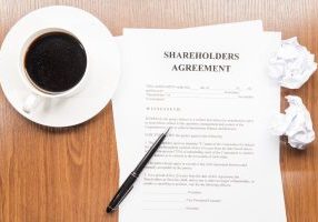 shareholders agreement document sitting on a wooden desk surrounded by a coffee cup, crumpled up paper and a pen