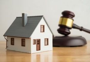House model, hammer judge gavel on wooden table with white wall background.