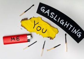 Word Gaslighting, on a black surface, next to a lighter with the word Me, and burnt yellow card with the writing You.