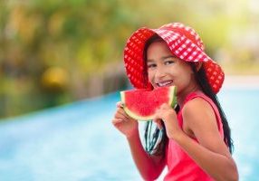 Child with watermelon in swimming pool. Summer sun and water fun. Healthy fruit snack for kids. Tropical fruits in family vacation. Travel with children. Little girl on beach holiday.