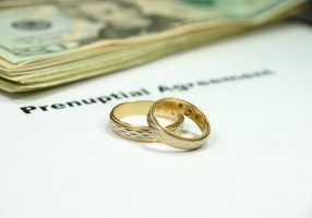 Two golden rings and a stack of US 20 dollar bills sitting on top of a white piece of paper with Prenuptial Agreement in black type.