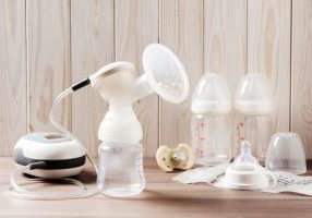 Breast pump and blank baby bottle on wood background