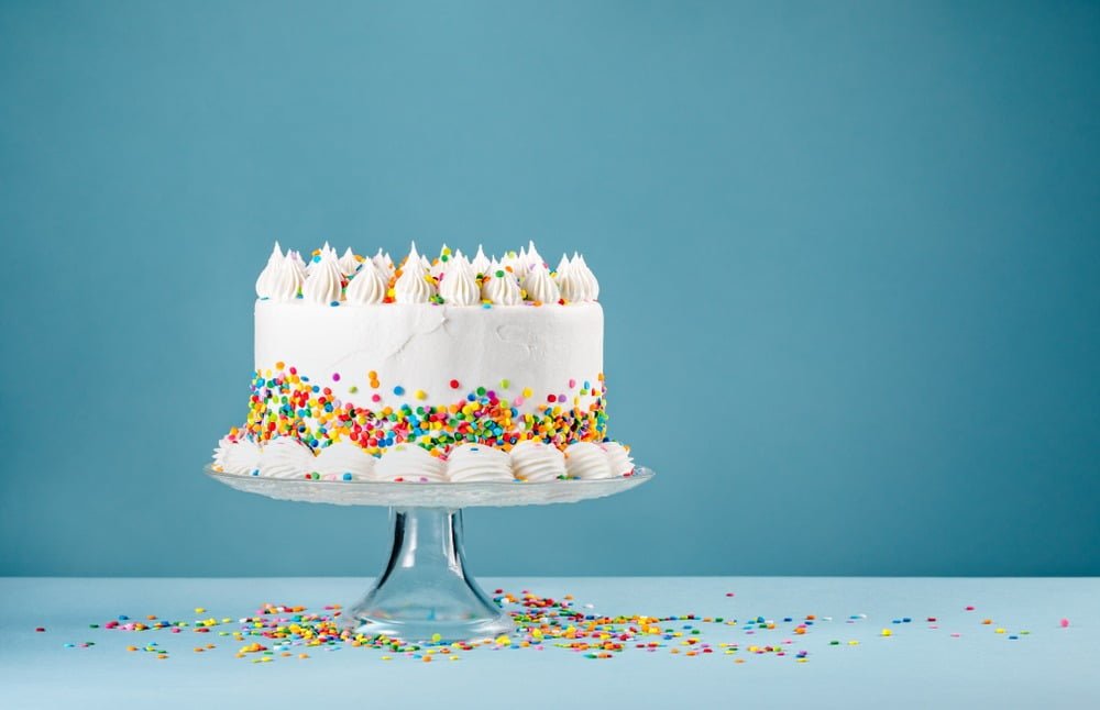 white simple birthday cake with colored sprinkles with a sky blue background.