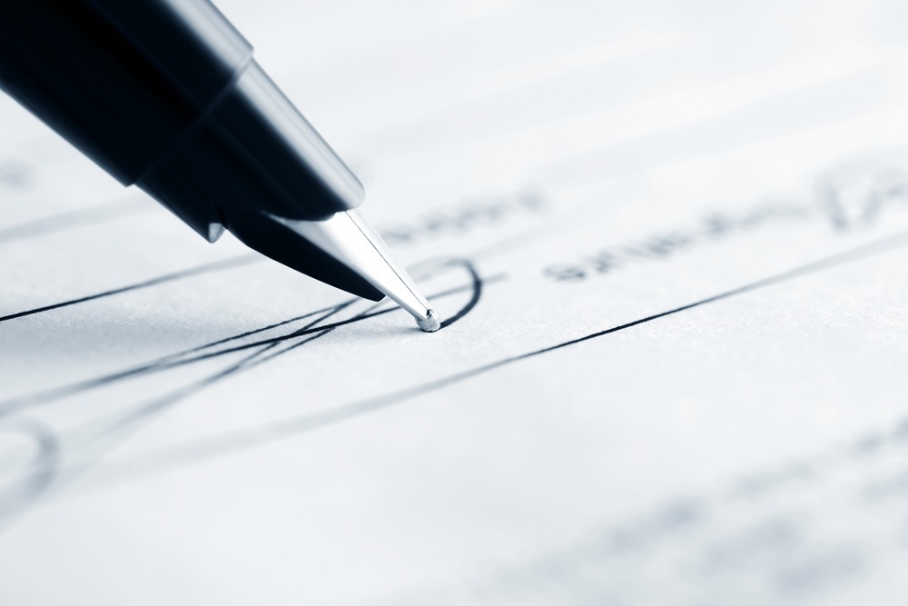 close up of a ballpoint black ink pen signing a formal document on white paper