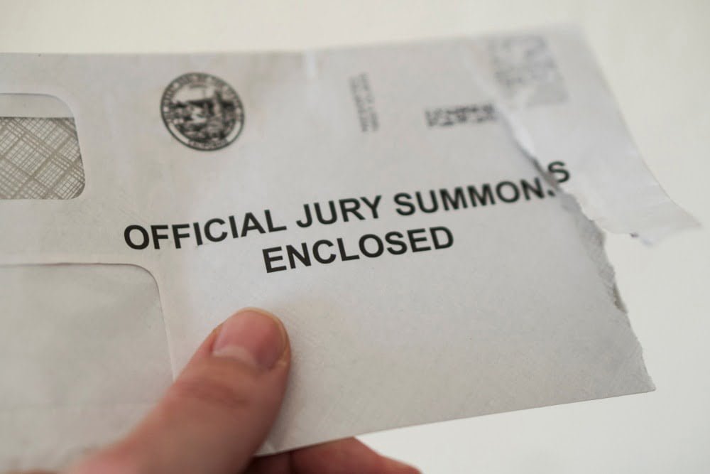 Closeup of open jury duty summons envelope, hand holding letter with white background, juror receiving notice. B
