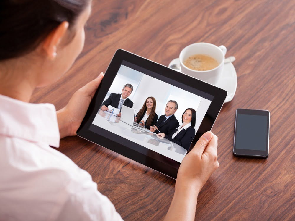 Woman looking at an ipad that has a pic of 4 people in a business meeting