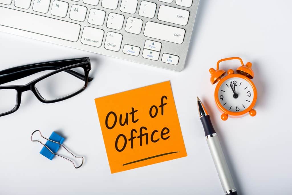note with out of office written on it sitting on a desk surrounded by office supplies