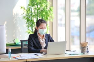 Female employee wearing medical facial mask while working alone because of social distancing policy