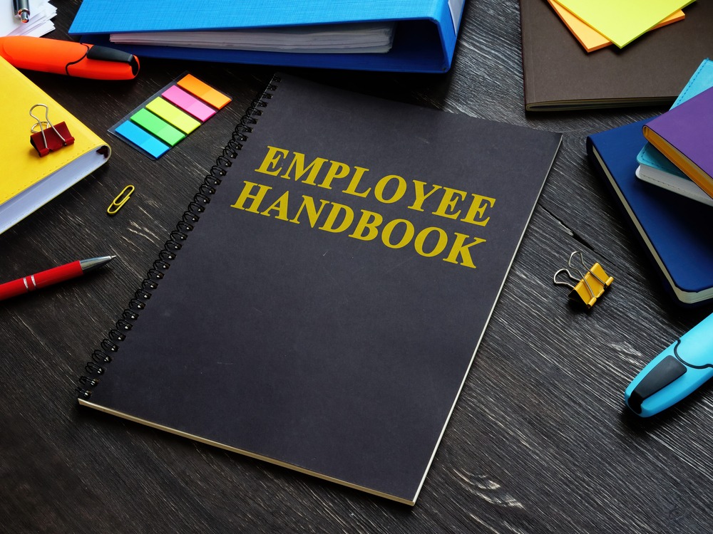 Employee handbook surrounded by office supplies on a dark wooden desk