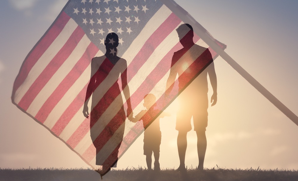 Happy family walking together at sunset holding hands against the American Flag