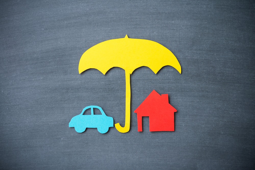 Paper cutout of car and house under yellow umbrella on blackboard background.