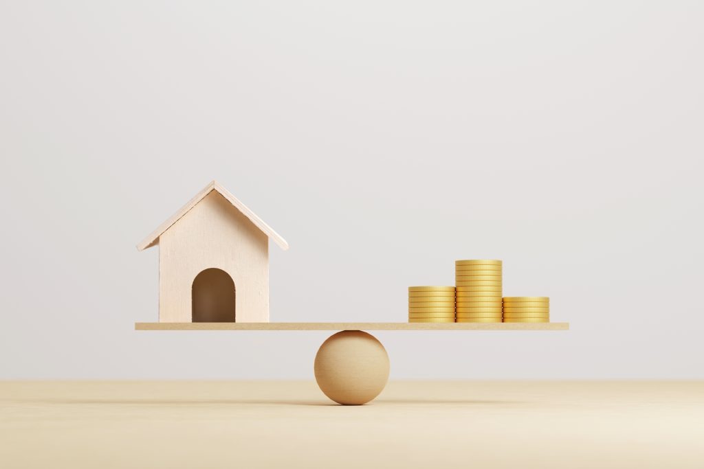 Wooden home and money coins balanced on wood scale.