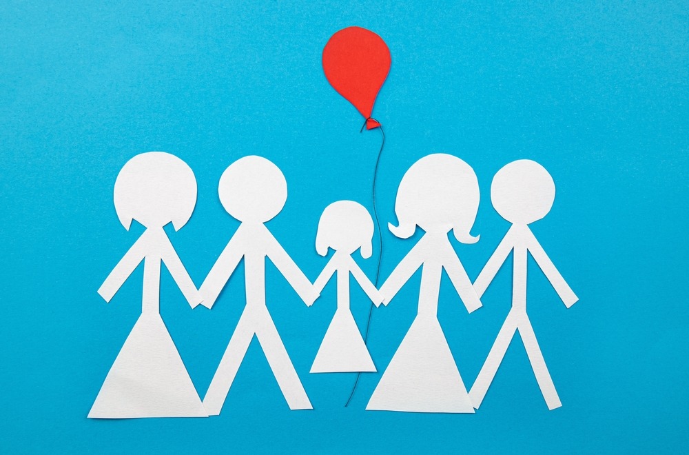 Conceptual image of co parenting. Two families sharing custody and parenting together. Two couples sharing a child with red balloon, cut out from paper, blue background. Or cluster families concept.