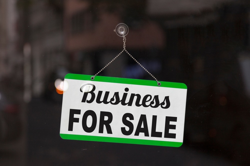 Close-up on a blue open sign in the window of a shop displaying the message: Business for sale.