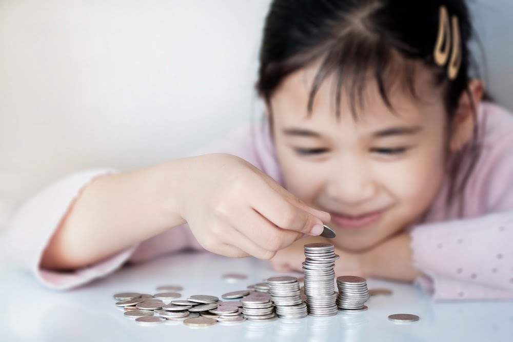 small female child smiling and counting up her savings and stacking coins.