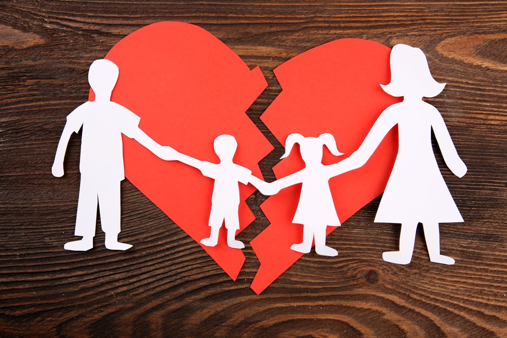 Paper cutout silhouette of a family split apart on a paper heart, divorce concept