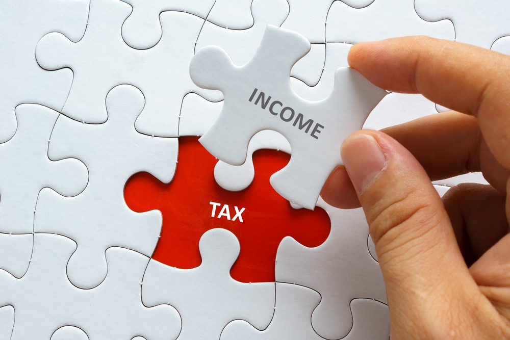 Hand holding piece of jigsaw puzzle with word INCOME TAX.