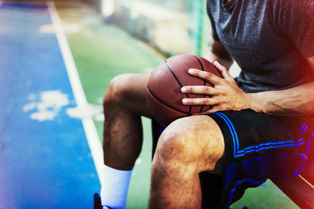 Young athlete sitting on an outdoor basketball court, holding a basketball in their hands, wearing sports attire