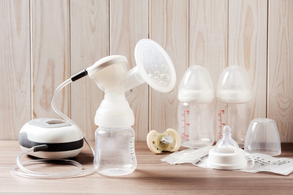 Breast pump and blank baby bottle on wood background
