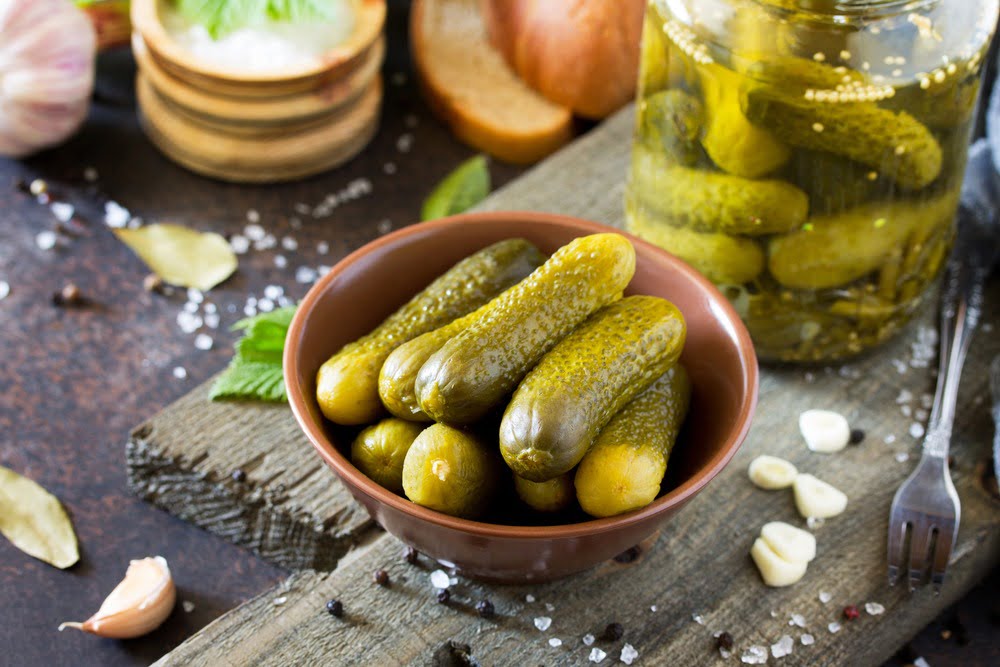 Green pickles in a tan bowl with ingredients in the background