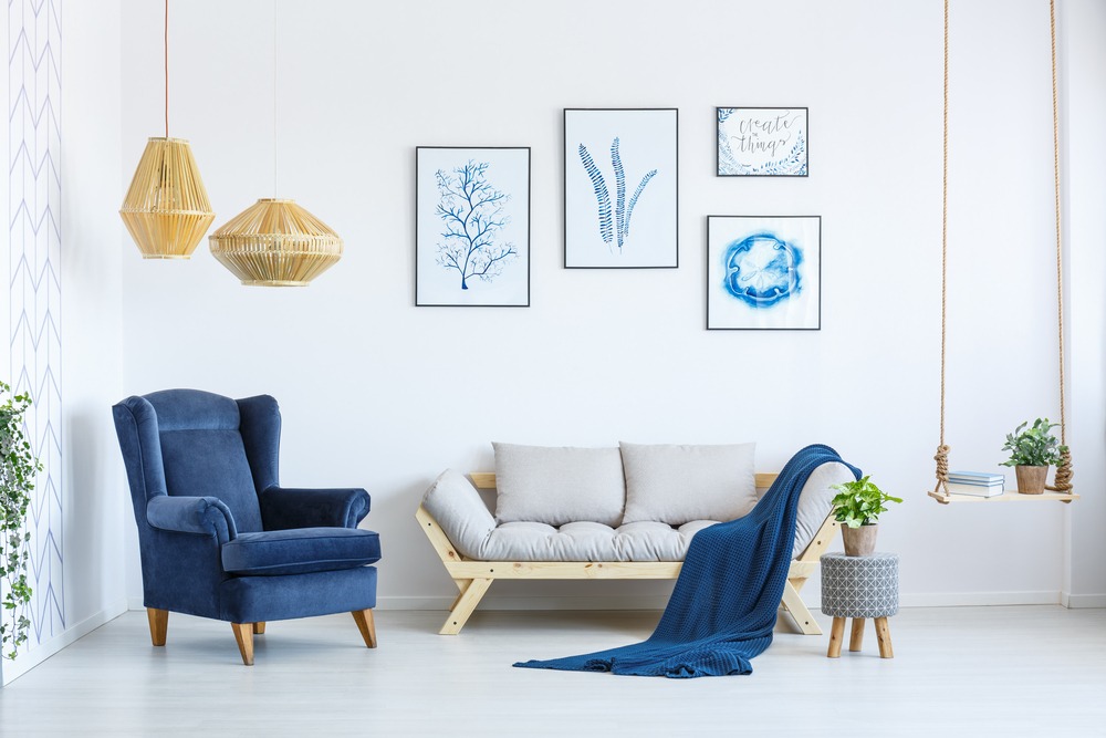White sofa and blue armchair in living room with posters on the wall