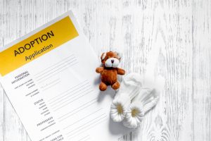 Adoption application near toy on light wooden table background top view copyspace