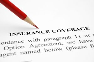 Red pencil hovering over "INSURANCE COVERAGE" typed in bold letters on a white piece of paper.
